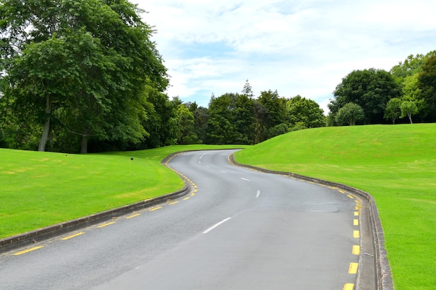 Asphalt road surrounded by bright green hills and trees during daylight