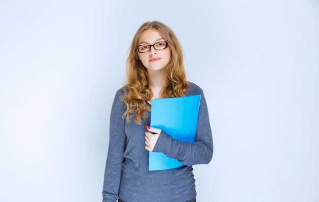 Assistant with eyeglasses holding a blue reporting folder.