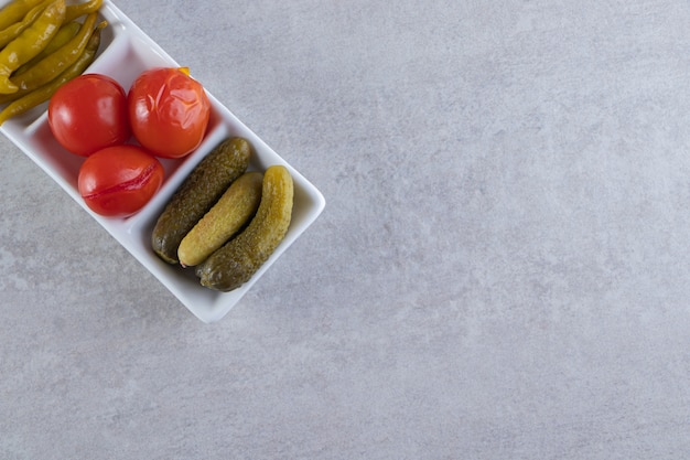 Assorted pickles vegetables placed on a stone background.