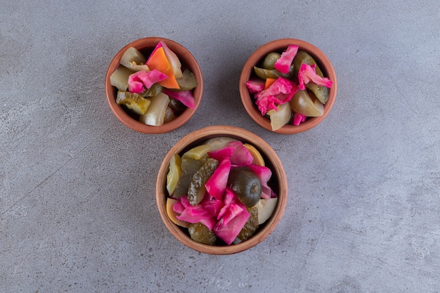 Assorted pickles vegetables placed on a stone surface.