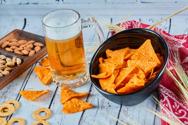 Free photo assorted snacks, chips, and a glass of beer on blue table.