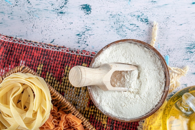 Free photo assortment of raw pasta in wooden basket with flour and oil.