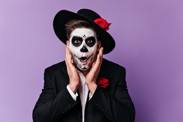 Astonished gentleman in hat with rose opened his mouth in amazement. Closeup portrait of man with painted face for carnival.