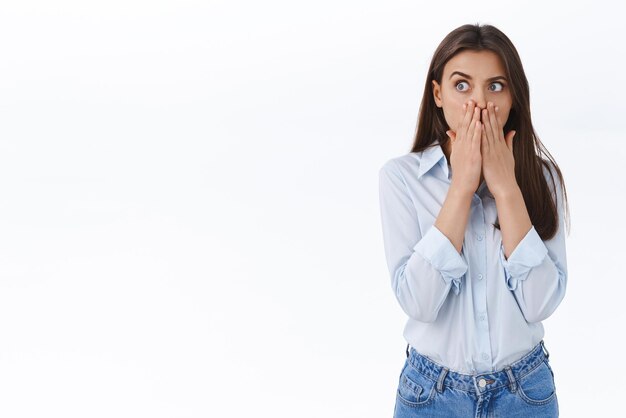 Astonished and shocked young woman overheard shocking information gossiping at office cover mouth with hands as gasping from amazement look left startled white background