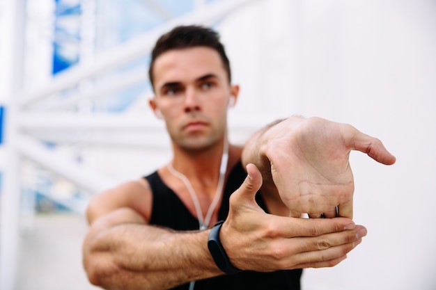 Free Photo athlete male in earphones while stretching his arms, preparing to workout outdoors.