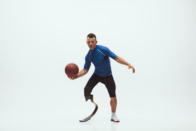 Athlete with disabilities or amputee isolated on white studio space. Professional male basketball player with leg prosthesis training and practicing in studio.