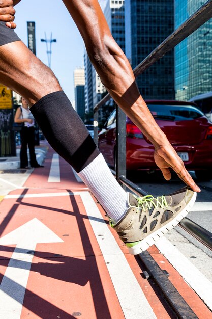 Athlete young man stretching his leg and hand on sidewalk in the city