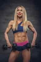 Free photo athletic blonde fitness model posing with dumbbells on grey background.