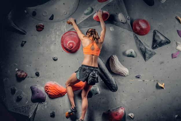 Athletic brunette female on indoor climbing wall.