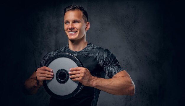 Athletic male holds a barbell weight in his arm over grey background.