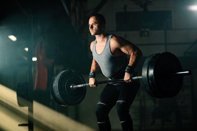 Free photo athletic man exercising with barbell during cross training in health club