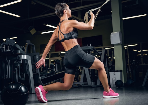 Free photo athletic middle age female with short hair doing legs workouts with trx suspension strips in a gym club.