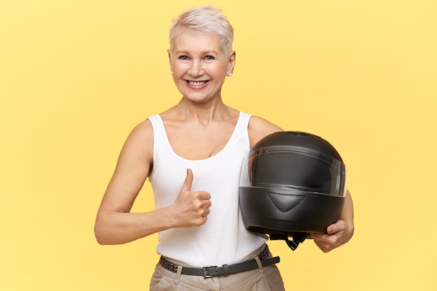 Free photo athletic middle aged woman with blonde hair holding protective motorcycle helmet