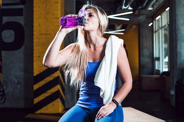 Free photo an athletic woman drinking water in gym