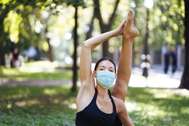 Athletic young woman in a medical protective mask, doing yoga in the Park in the morning, women's training on a yoga Mat