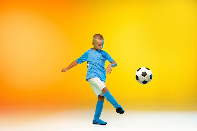 Free Photo attack. young boy as a soccer or football player in sportwear practicing on gradient yellow in neon light