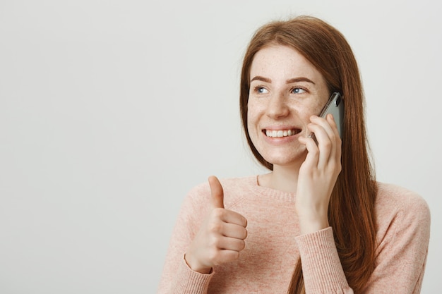 Free photo attactive smiling redhead woman talking on mobile phone and show thumb-up