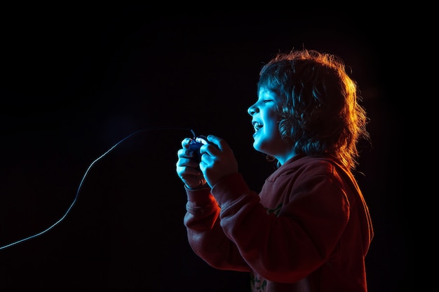 Free photo attented playing videogames. caucasian boy's portrait on dark  wall in neon light. beautiful curly model. concept of human emotions, facial expression, sales, ad, modern tech, gadgets.