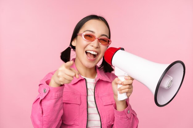 Attention announcement concept Enthusiastic asian girl shouting in megaphone advertising with speaker recruiting standing over pink background