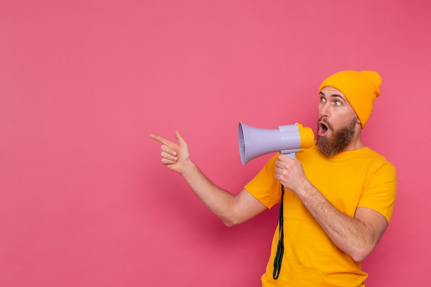 Free photo attention! european man with megaphone pointing finger to the left on pink background