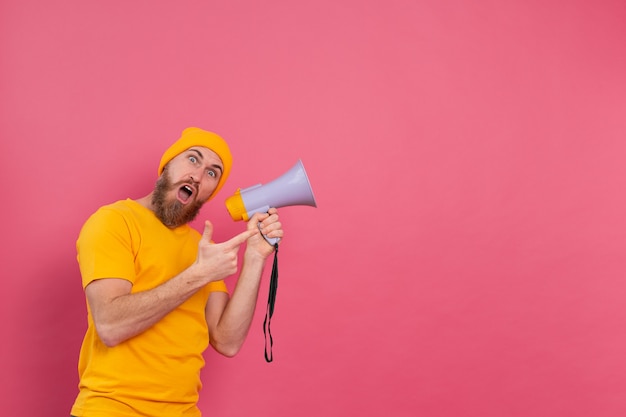 Free Photo attention! european man with megaphone pointing finger to the right on pink background