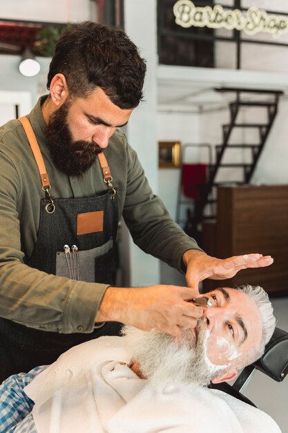 Attentive barber shaving beard to client in barber shop