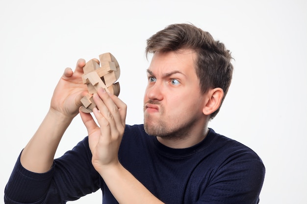 Attractive 25 year old business man looking confused with wooden puzzle.