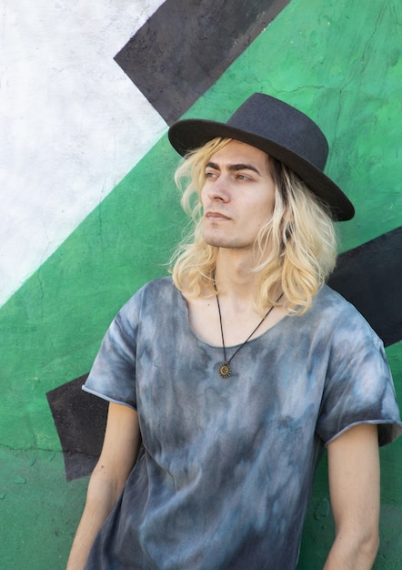 Free Photo attractive armenian guy with a hat leaning on a blue and green wall and looking away