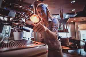 Free photo attractive barista in uniform is prepairing coffee for customers using new coffee maker.