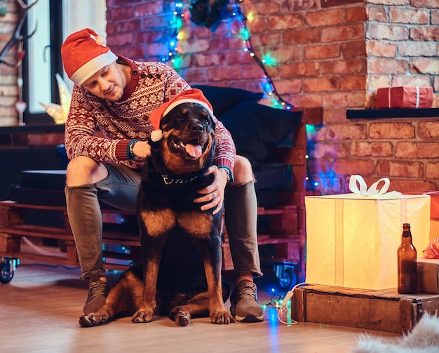 Free Photo attractive bearded hipster male with his rottweiler dog in a room with christmas decoration.