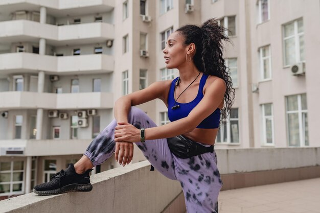 Attractive black african american woman in sport fitness urban outfit on rooftop making work out confident curly hair style athletic body strong muscles