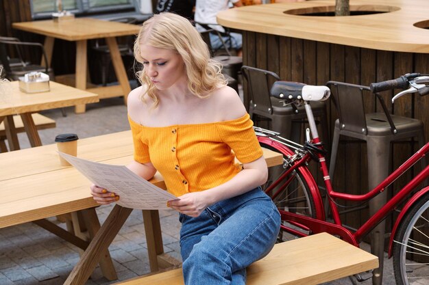 Attractive blond girl sitting in courtyard of cafe while thoughtfully reading menu