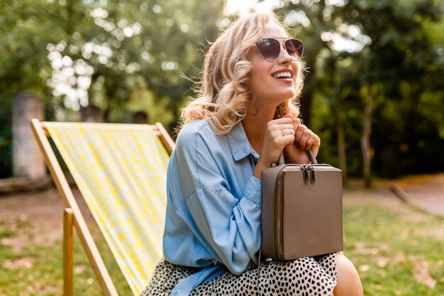 Attractive blond smiling woman sitting in deck chair in summer outfit