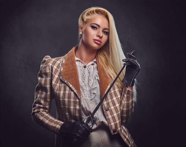 An attractive blonde female dressed in medieval urban clothes holds a silver sword over grey background.