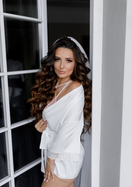 Free Photo attractive brunette caucasian bride with curly hair is looking straight dressed in white silk nightgown