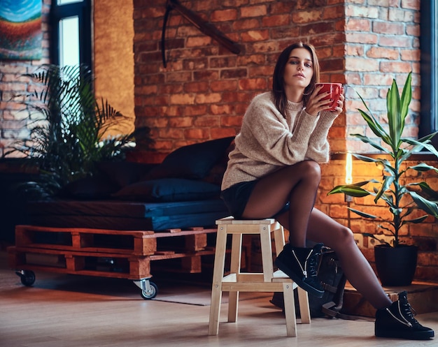 Attractive brunette female posing near the window in a room with loft interior.