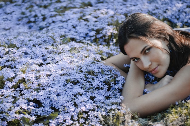 Free photo attractive brunette woman with sexy look is lying on the yard with blue flowers