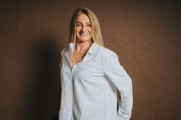 Attractive caucasian blonde female in a white shirt posing on a brown background