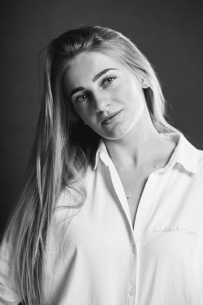 An attractive caucasian blonde female in a white shirt posing on a brown background