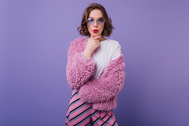 Free Photo attractive caucasian woman in bright attire with surprised face expression. indoor portrait of refined curly female model in pink fur coat.