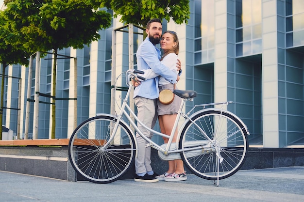 Attractive couple on a date after bicycle ride in a city. A man hugs a woman over modern building background.