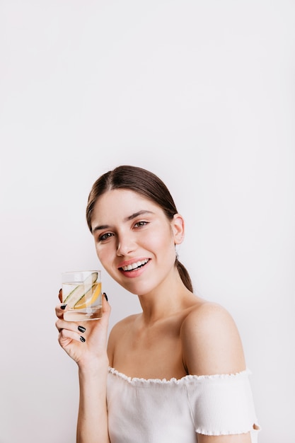 Attractive dark-haired woman is full of energy and smiles. Lady holding glass of water with lemon.