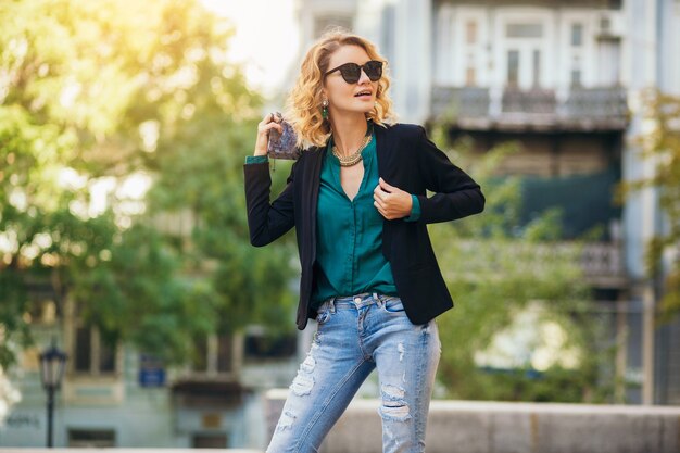 Attractive elegant woman walking in city street with purse, wearing black jacket, confident and sexy,