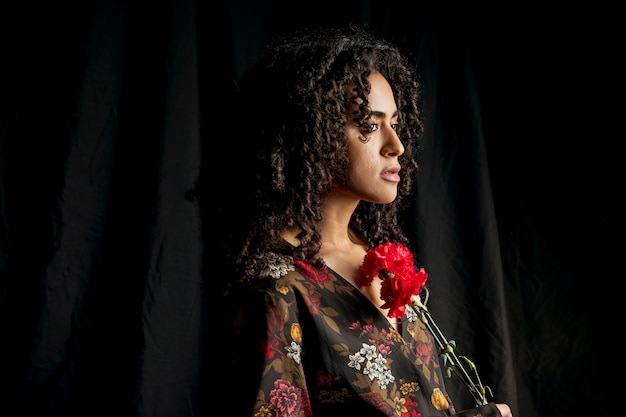 Attractive ethnic woman with red flowers in dark 