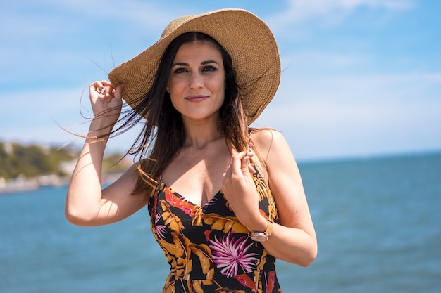 Attractive female in a floral dress and a hat captured by the beautiful sea in Spain