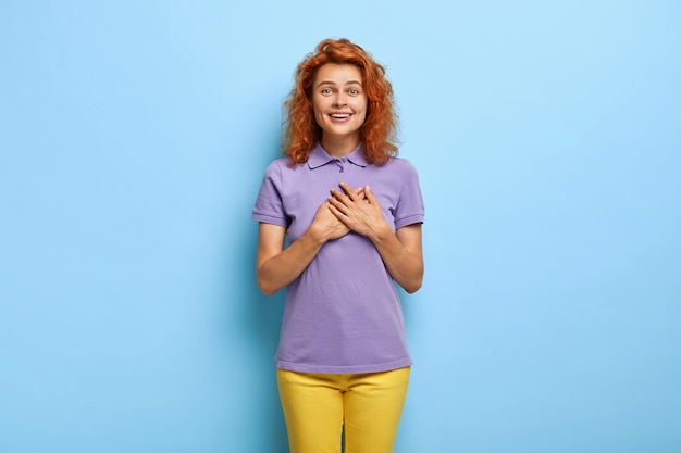 Free Photo attractive ginger girl presses hands on chest, feels gratitude