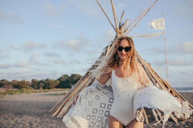 Free photo attractive girl in black glasses posing with interested smile at beach outdoor portrait of happy longhaired woman wears white swimwear