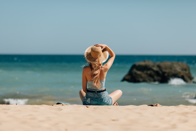 Attractive girl in sunglasses and hat lies on warm sand