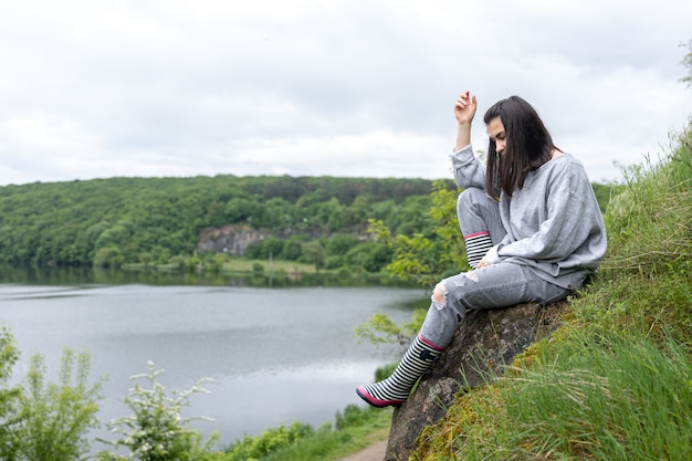 An attractive girl on a walk climbed a cliff in a mountainous area and enjoys the scenery.