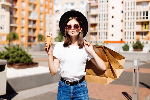 Attractive girl walking with ice cream holding shopping bags in shopping mall